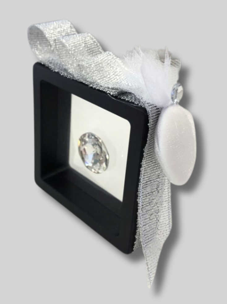 DIAMANTE PREZIOSO IN SCATOLA CON BORDO NERO SFONDO TRASPARENTE CON NASTRO ARGENTATO E CONFETTO CON PICCOLO PREZIOSO